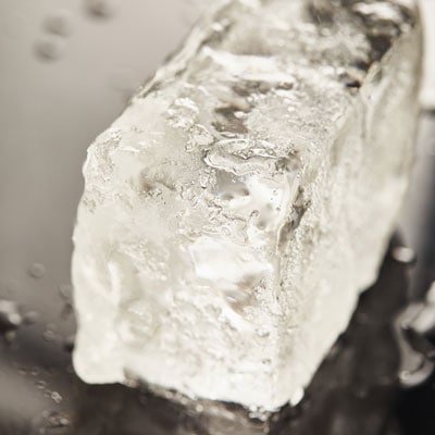 A close-up of an ice cube melting on a reflective surface, emphasizing freshness and cold storage solutions.